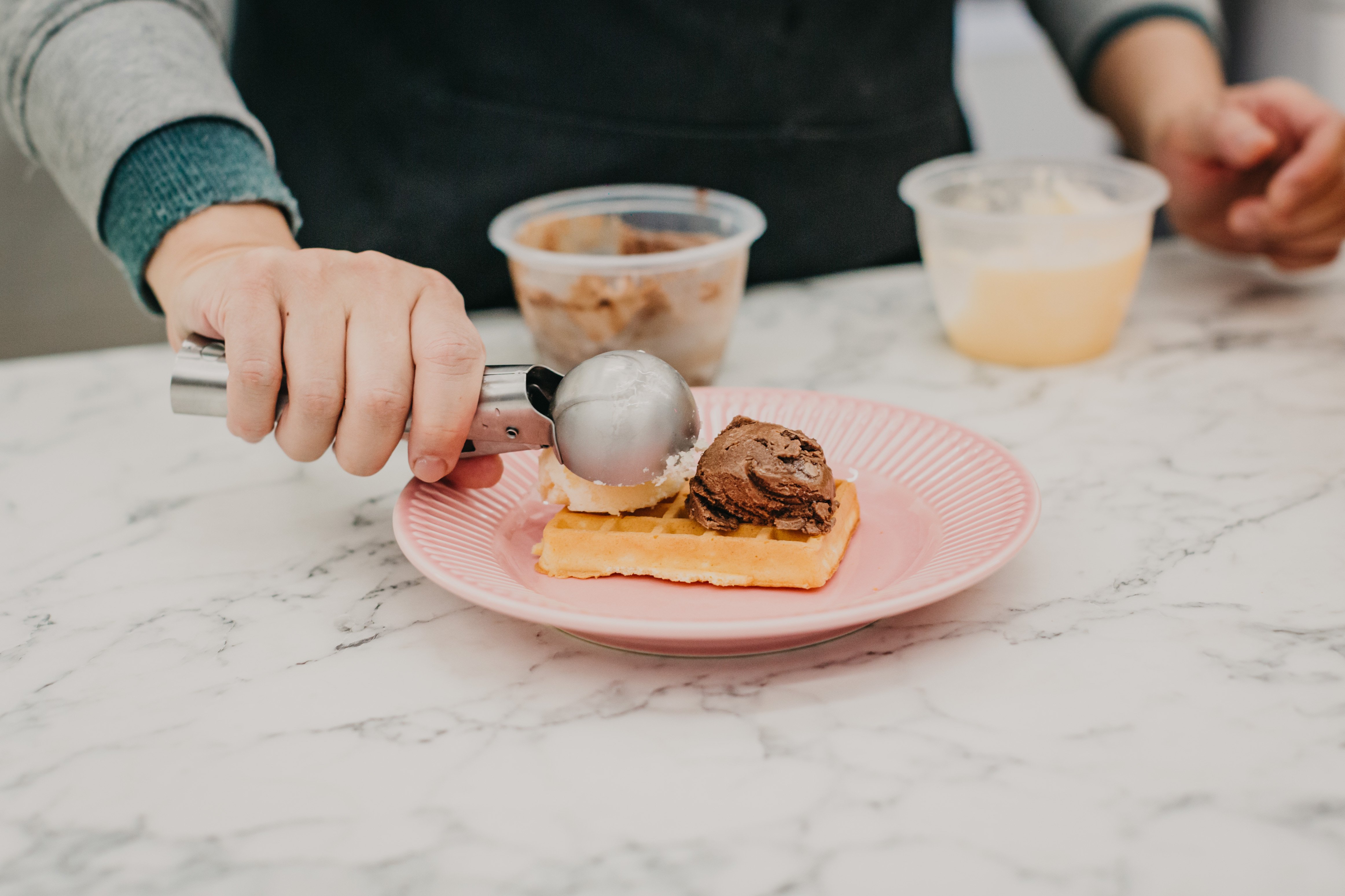 Person adding scoops of ice cream to a waffle